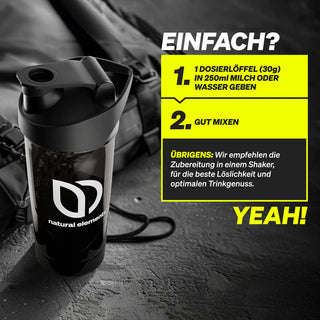 Eine schwarze Shaker-Flasche mit dem "natural elements"-Logo steht neben einer Tüte. Eine Anleitung auf Deutsch beschreibt, wie man das Pulver mit Milch oder Wasser mischt und empfiehlt die Verwendung eines Shakers.